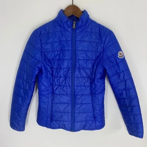 Blå dunjacka från Moncler - Blå dunjacka från Moncler med dragkedja och hög krage. Storlek 0 som är XS enligt Moncler. Passar runt 160cm långa. Reva inuti jackan se bild 5 men annars väldigt fin. Revan bidrar till det låga priset. Unisex!
