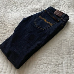 Nudie jeans  - Snygga mörkblå jeans med kontrasterande gul söm på bakfickorna. De har en klassisk femficksdesign och en bekväm passform. Perfekta för en stilren look. Märke nudie jeans. I storlek W32 L34