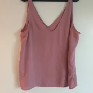 Rosa ärmlös linnetopp - Säljer en stilren rosa linnetopp med v-ringning. Toppen är ärmlös och har en lös passform, perfekt för varma dagar. Den mjuka färgen gör den lätt att matcha med olika outfits.