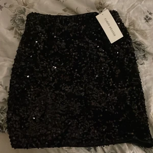 Svart paljettkjol från Carin Wester - Snygg svart kortkjol från Carin Wester täckt med glittrande paljetter. Perfekt för att sticka ut med en glittrig look. Kjolen har en tight passform och är i storlek XS. Den är helt ny med prislappen på och har aldrig använt den, köpte den för 500kr.