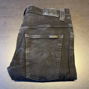 Nudie Jeans - Snygga svarta jeans från Nudie Jeans med klassisk femficksdesign. De har en knappgylf och märkets logga på bakfickan. Perfekta för en stilren look. 31w men passar mindre