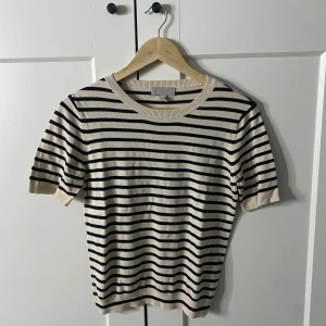 Randig kortärmad tröja från H&M - Säljer en stilren randig tröja från H&M i beige och svart. Tröjan har korta ärmar och en rund halsringning, perfekt för en avslappnad look. Passar bra till både jeans och kjol.