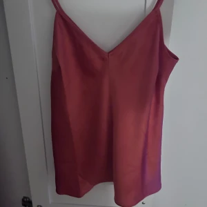 Glansig topp  - Säljer en stilren glansig topp med smala axelband och v-ringning. Perfekt för varma dagar eller sommarens fester. Toppen har en enkel och elegant design som gör den lätt att matcha med olika accessoarer.