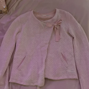 Rosa kofta från Odd Molly - Säljer en söt rosa kofta från Odd Molly med en fin rosett på framsidan. Koftan har ett diskret mönster och två fickor. Perfekt för en mysig dag.
