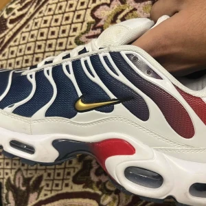 Nike Air TN i blått, rött och vitt - Snygga Nike Air TN med en iögonfallande design i blått, rött och vitt. Skorna har den klassiska Tn Air-dämpningen och en vågig överdel med vita detaljer. Perfekta för dig som vill ha en unik stil.