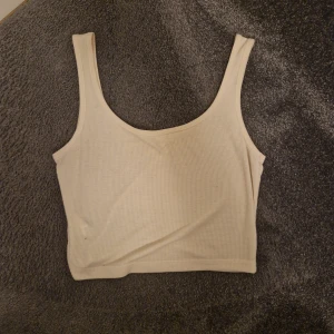 Vit ribbad linnetopp - Säljer en stilren vit ribbad linnetopp. Perfekt för varma dagar med sin ärmlösa design och mjuka material. Enkel att matcha med olika outfits.