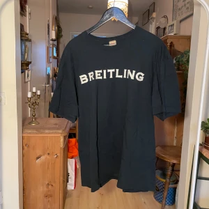 Svart t-shirt från Breitling - Säljer en svart t-shirt från Breitling med stort tryck av en helikopter och texten 'INSTRUMENTS FOR PROFESSIONALS' på baksidan. Framsidan har Breitling-loggan i vitt. Köpt på herr Judit 