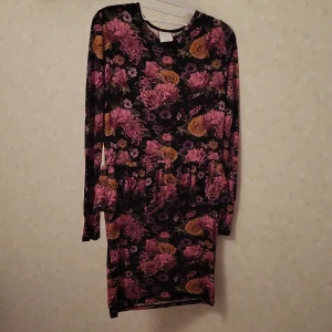 Blommig klänning med långa ärmar - Snygg blommig klänning med långa ärmar i en mix av rosa, lila och gula blommor på en svart bakgrund. Perfekt för en färgglad look!