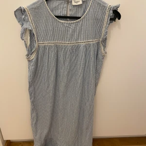 Randig klänning från Saint - Söt randig klänning från Saint i blått och vitt. Klänningen har korta ärmar med volangdetaljer och en rund halsringning. Perfekt för en avslappnad sommarlook.