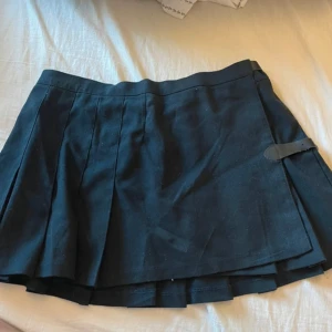 Svart kjol från Brandy Melville - Snygg svart kortkjol från Brandy Melville med knappar och bältesdetalj. Perfekt för en stilren look.