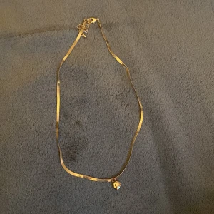 Guldhalsband med pärldetalj - Elegant guldhalsband med en liten pärldetalj som hänge. Halsbandet har en tunn kedja och ett diskret lås.