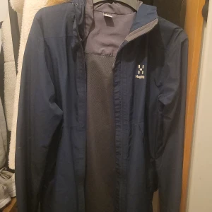 Blå vindjacka från Haglöfs - Säljer en blå vindjacka från Haglöfs med dragkedja och huva. Perfekt för blåsiga dagar och utomhusaktiviteter. Jackan har en stilren design och är långärmad. Använd några gånger, storlek S.