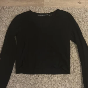 Svart långärmad tröja - Säljer en stilren svart långärmad tröja med v-ringning. Perfekt för lager-på-lager eller som den är. Enkel och mångsidig design.