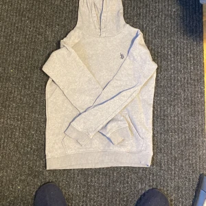 Grå polo hoodie - Säljer en stilren grå hoodie från polo. med broderad logga på bröstet. Tröjan har långa ärmar och en bekväm huva, perfekt för en avslappnad look