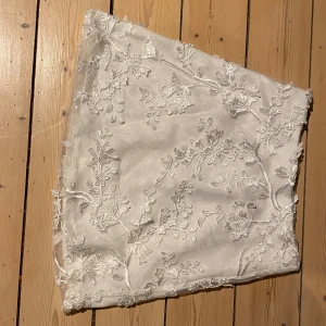 Vit kjol med spets från Bik Bok - Elegant vit kjol från Bik Bok i storlek XS. Kjolen är dekorerad med vacker spets i blommönster, perfekt för en stilren look. Den har en kort längd och är tillverkad i ett lätt material som ger en luftig känsla.