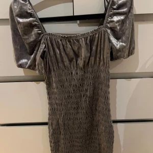 Grå klänning med puffärmar - Snygg grå klänning med puffiga ärmar och smockdetaljer. Klänningen har en unik textur och är tillverkad i ett glansigt material. Perfekt för finare tillfällen, köpte den utomlands så tror inte den finns i Sverige! Köpte den för 299kr säljer den för 150+ frakt. Passar nog de flesta storlekarna eftersom den är stretchig material