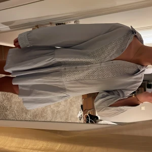 Ljusblå klänning från Zara - Säljer en söt ljusblå klänning från Zara med broderade detaljer längs framstycket och ärmsluten. Klänningen har långa ärmar och en avslappnad passform med en lätt volang vid kjolen. Perfekt för vår och sommar! Använd en gång, priset kan diskuteras!❤️