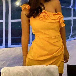 Orange offshoulder klänning - Trendig organe från mango, offshoulder klänning med volangdetaljer. Perfekt för sommarens fester med sin korta längd och figurnära passform.