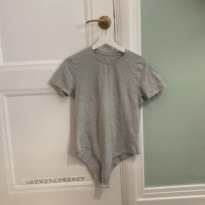 Grå stretch body från Primark - Säljer en grå stretch body från Primark. Den har korta ärmar och en rund halsringning. Perfekt för en enkel och bekväm stil.