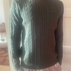 Grön kabelstickad tröja från Brandtex - Säljer en stilren grön kabelstickad tröja från Brandtex. Tröjan har en klassisk rund hals.Modell 185 cm 76 kg 
