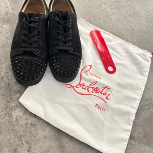 Svarta sneakers från Christian Louboutin - Snygga svarta sneakers från Christian Louboutin med coola nitar på tån och snörning. Perfekta för att ge din outfit en edgy touch.