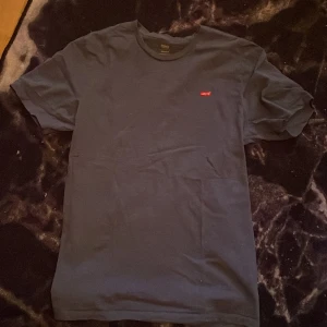 Mörkblå t-shirt från Levi's - Säljer en mörkblå t-shirt från Levi's med röd logga på bröstet. T-shirten är kortärmad och tillverkad i bomull, perfekt för en avslappnad stil.