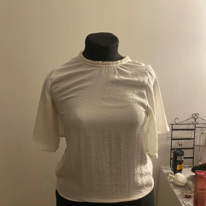 Vit blus med korta ärmar - Säljer en stilren vit blus med korta ärmar. Blusen har en rund halsringning och är tillverkad i ett lätt och luftigt material, perfekt för varmare dagar.
