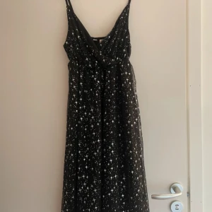 Svart klänning med stjärnmönster från Bodyflirt - Snygg svart klänning från Bodyflirt med ett glittrande stjärnmönster. Klänningen har smala axelband och en v-ringad design som ger en elegant look. Perfekt för en stjärnklar kväll!