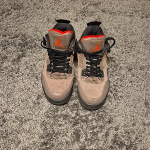 Nike Air Jordans i mocka och syntet - Snygga Nike Air Jordans i beige och svart med orange detaljer. Skorna har snörning och är tillverkade i en kombination av mocka och syntetmaterial. Perfekta för en stilren look.
