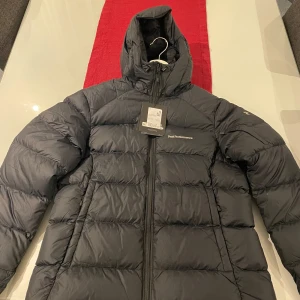 Svart dunjacka från Peak Performance - Oanvänd helt ny svart dunjacka från Peak Performance med dragkedja och huva. Modell frost down strl medium. Alla lappar kvar