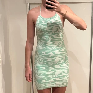 Grön och vit mönstrad klänning - Trendig grön och vit klänning med ett unikt mönster. Klänningen är ärmlös och har en tight passform som framhäver figuren. Perfekt för sommarens alla tillfällen.