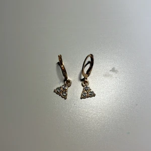 Guldörhängen med triangelformade hängen - Eleganta guldörhängen med triangelformade hängen dekorerade med små gnistrande stenar. Perfekta för att ge en touch av glamour till din stil. Lätta att bära med en säker låsmekanism.
