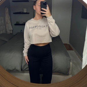 Puderrosa croppad tröja med tryck - Säljer en puderrosa croppad tröja med texten 'California EST. 1997' på framsidan. Tröjan har långa ärmar och en avslappnad passform, perfekt för en casual look. Den är mjuk och bekväm att bära. Aldrig använd och liten i storleken 