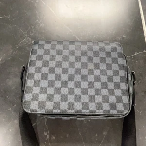 Rutig axelväska - Snygg axelväska med ett klassiskt rutigt mönster i grått och svart. Väskan har en praktisk dragkedja och en justerbar axelrem. Perfekt för att bära med sig det nödvändigaste med stil.