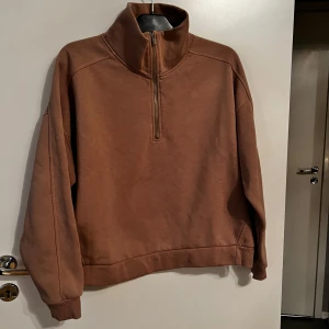 Brun fleece tröja med dragkedja från 157 - Säljer en brun fleece tröja från 157 med halv dragkedja och hög krage. Perfekt för kyliga dagar med sin mjuka och varma insida. Tröjan har långa ärmar och en avslappnad passform.