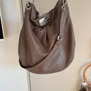 Marc Jacobs väska - Marc Jacobs väska i modellen Too hot to handle. Väskan är grå/beige och har silvriga detaljer. Väskan är i superfint skick och har inga slitningar.