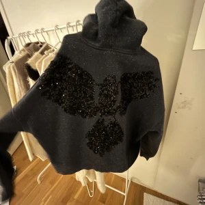 Svart hoodie med paljettmönster - Snygg svart/mörkblå hoodie från other storys. Perfekt för att ge din outfit lite extra bling. Den har en bekväm passform!
