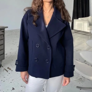 Mörkblå kappa med knappar - Snygg mörkblå kappa med dubbelknäppning och bred krage. Perfekt för kyligare dagar och ger en stilren look. Passar bra till både jeans och klänning.