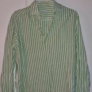 Grön- och vitrandig skjorta från Soloio - Snygg grön- och vitrandig skjorta från Soloio med klassisk krage och knappar framtill. Skjortan har långa ärmar och är perfekt för en stilren look, både knäppt som uppknäppt. Storlek xs men skulle säga att den är oversized, passar både män o kvinnor:) nypris runt 2500