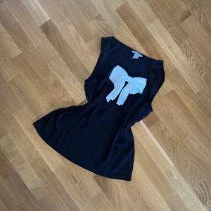 Svart ärmlös topp med vit rosett - Snygg svart ärmlös topp från H&M med en stor vit rosett framtill. Mjukt och bekvämt material. Endast använd 1 gång