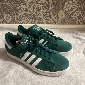 Gröna Adidas Campus sneakers - Snygga gröna Adidas Campus sneakers med klassiska vita ränder och snörning. Perfekta för en stilren och sportig look. Skorna är tillverkade i mocka och har en vit sula. Skorna är inte ens använda en gång. Köpte fel storlek sen har de blivit stående. Tror jag kan hitta org kartongen men inte säker. Lappen sitter kvar. 