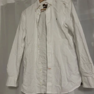 Vit skjorta med knappar - Klassisk vit skjorta med lång ärm och knappar framtill. Perfekt för en stilren look. Skjortan har en enkel design och är tillverkad i ett lätt material.