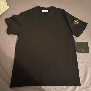Svart t-shirt från Stone Island - Snygg svart t-shirt från Stone Island med korta ärmar och det ikoniska märket på ärmen. Perfekt för en stilren look. Helt ny! Aldrig använd,  kommer med en lapp etikett från stone island 