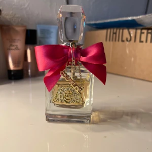 Parfym från Juicy Couture - Elegant parfymflaska från Juicy Couture med en lyxig design. Flaskan är dekorerad med en stor rosa rosett och ett gyllene emblem. Perfekt för den som älskar en feminin och glamorös stil.