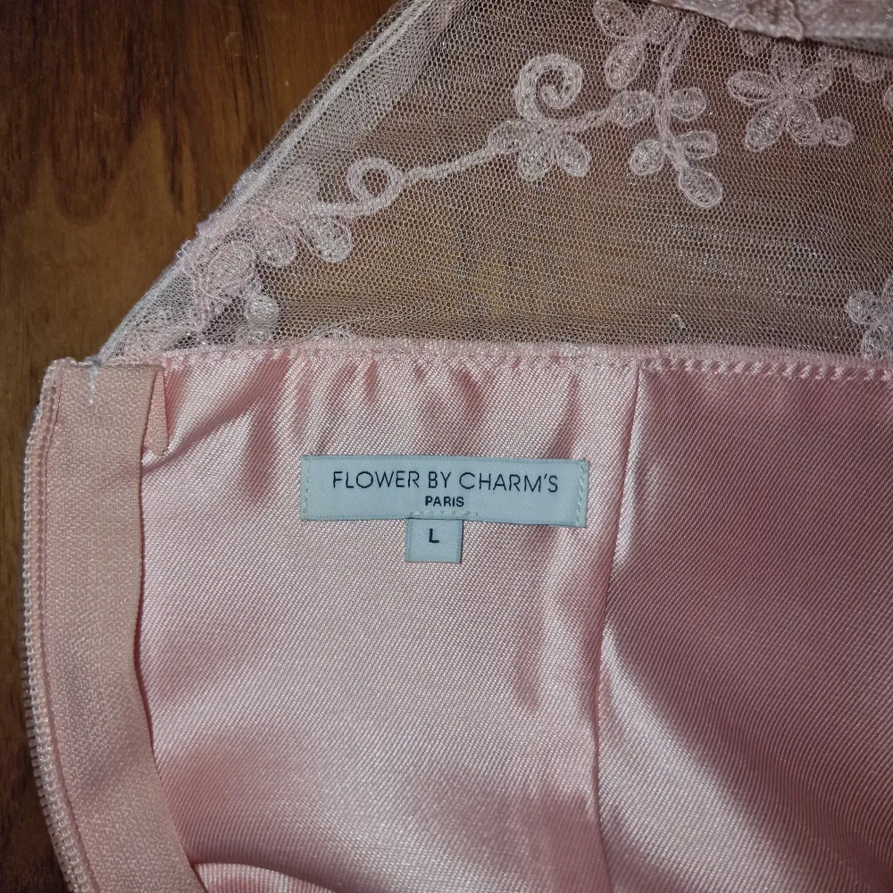 Charmig rosa klänning i satin med vackra spetsdetaljer och en elegant dragkedja i ryggen. Klänningen har en ärmlös design och en smickrande passform som passar perfekt för speciella tillfällen.. Mekot.