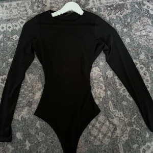 Svart långärmad bodysuit - Svart bodysuit med långa ärmar. Stretchigt material, mycket bekväm! Den har en öppen rygg med knytning. Strl xs. Bara använd vid ett tillfälle💗