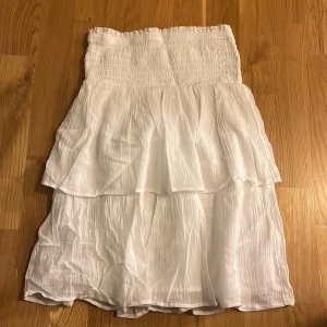 Vit kjol från Gina Tricot - Säljer en söt vit kjol från Gina Tricot med volanger. Kjolen har en smockad midja som ger en bekväm passform. Perfekt för varma dagar och kan stylas på många sätt. 🌸