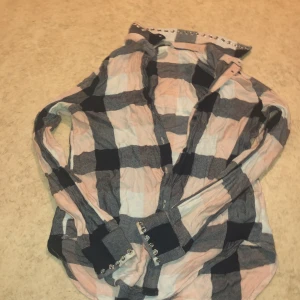 Rutig skjorta från H&M - Säljer en rutig skjorta från H&M i mjuka toner av rosa, blått och beige. Skjortan har långa ärmar och knappar framtill. Perfekt för en avslappnad stil med en touch av elegans. Passar bra till jeans eller kjol för en trendig look.