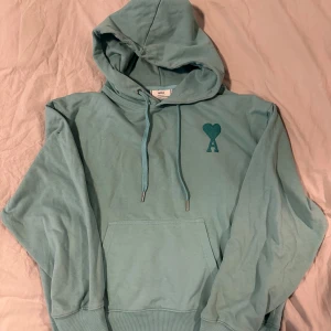 Ljusblå hoodie från Ami - Säljer en snygg ljusblå hoodie från Ami med en stilren design. Hoodien har en känguruficka och en liten hjärtdetalj på bröstet. Perfekt för en avslappnad stil.