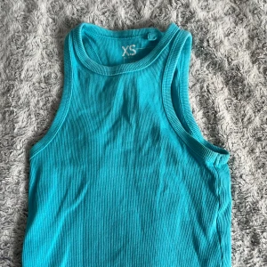 Turkos ribbad linnetopp från FSBN Sister - Säljer en snygg turkos ribbad linnetopp från FSBN Sister. Perfekt för varma dagar med sin ärmlösa design och mjuka material. Toppen är i storlek XS och har en stilren look.